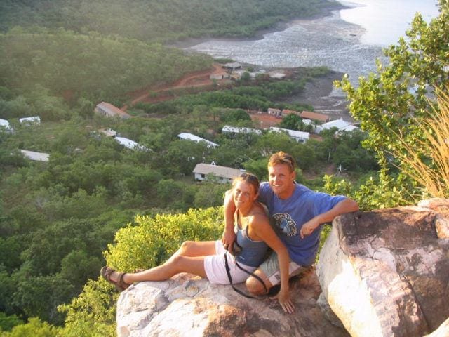 couple sitting on edge of cliff with views of kuri bay