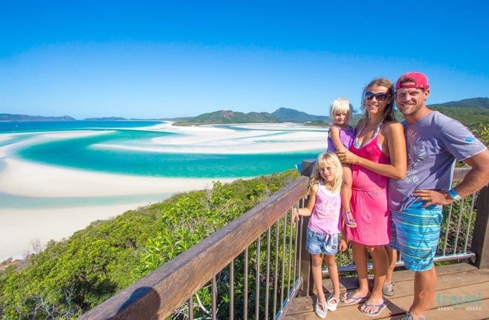 family posing in front of swirling white sand and blue waters of Whitehaven Beach