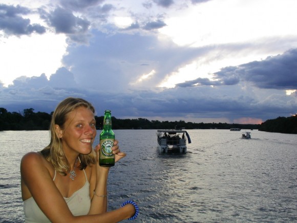 a woman holding a drink and standing next to a lake