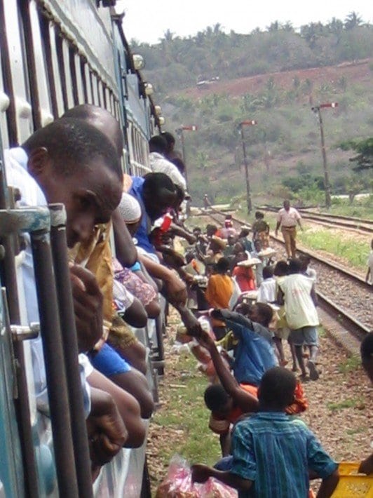 people hanging out train window with hawkers selling to them 