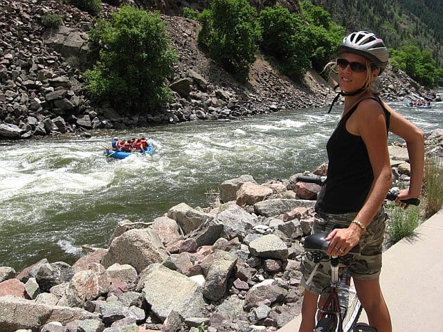 caz on bike beside colorado river with rafts going down