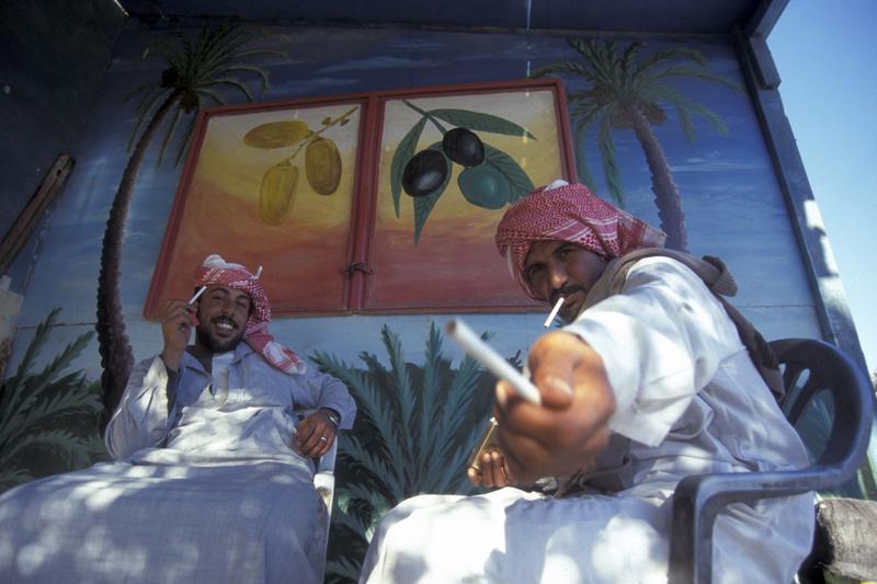 two Egyptian men with headdress offering a cigarette to camera