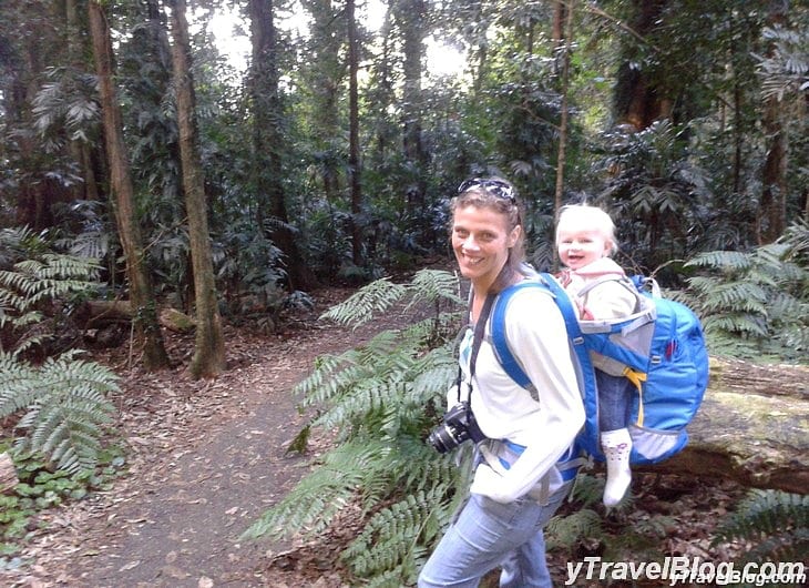 a woman carrying a baby through a forest trail