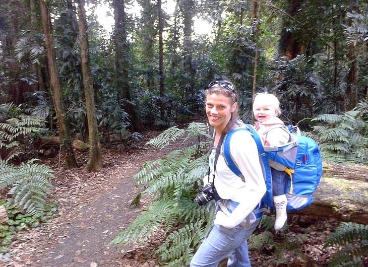 a woman carrying a baby on a trail