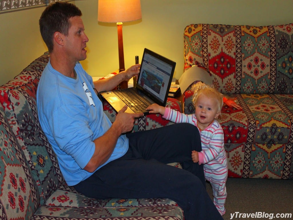 a man working on a computer while a child holds onto his leg