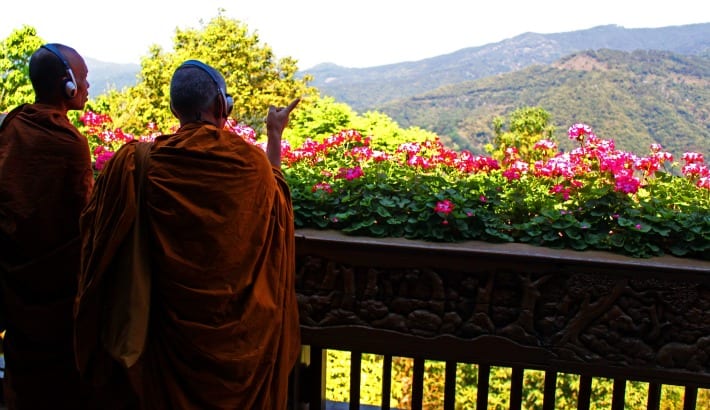 orange robed monks with headphones on looking at view of moutnains