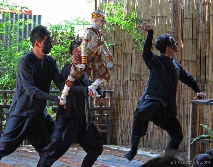 three men in black clothes with a thai puppet performing