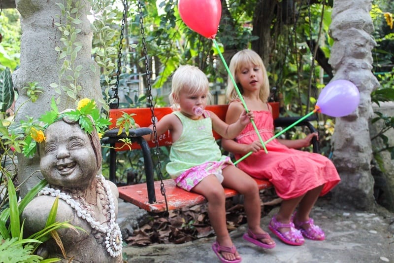 two young girls holding balloons sitting on bench in thai garden