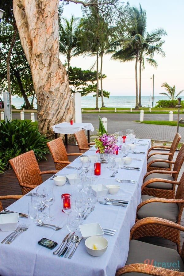table set on patio of Peppers Palm Cove Resort beside gum tree with views of the ocean.