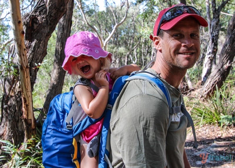 girl grinning in hiking carrier on dad's back