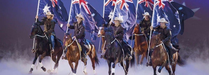 people riding on horses carrying australian flags