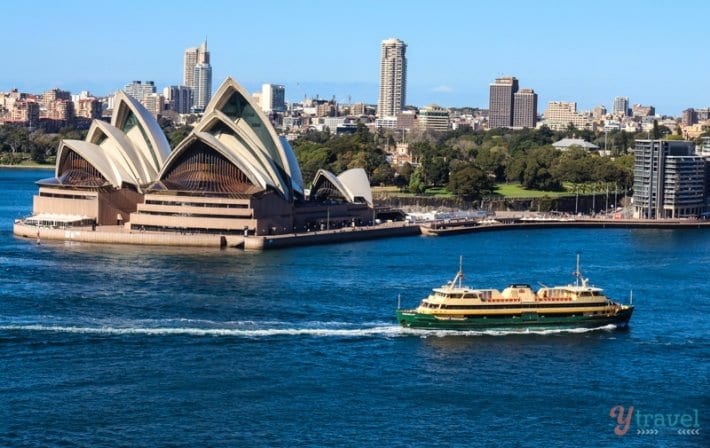 ferry passing the sydney opera house with the botanic gardens behind it
