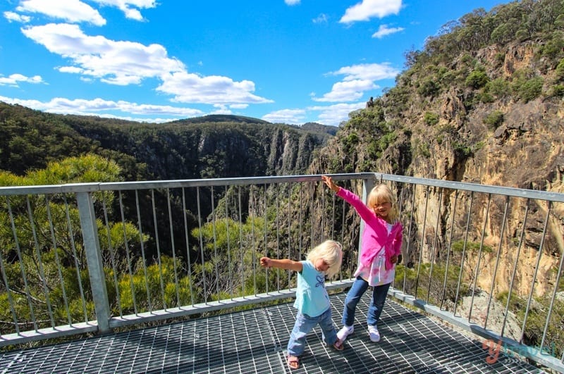 girls holding hands in air with view of Dangars Gorge 