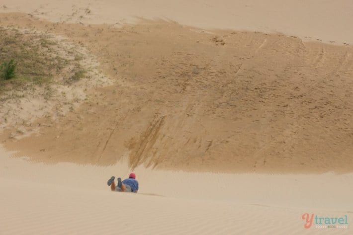 man sand boarding down a sand dune