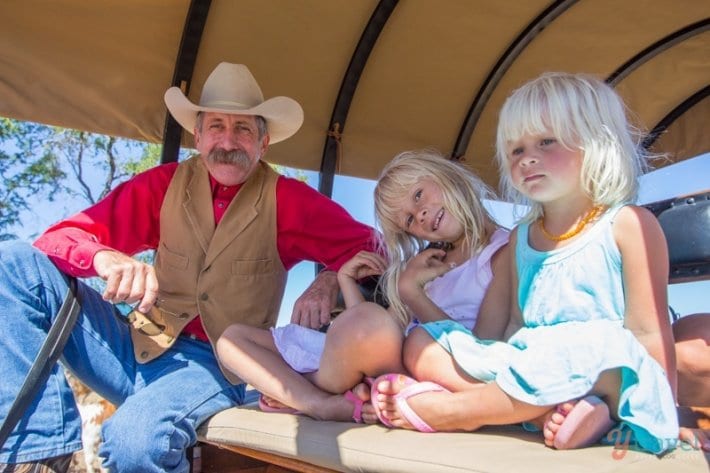kids sitting in a carriage next to a cowboy