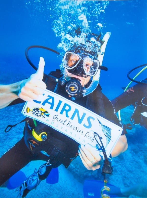 man underwater in scuba gear holding sign that says cairns 