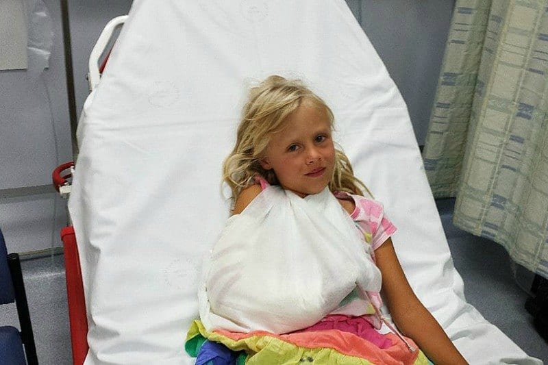 A little girl sitting on a bed with a broken arm
