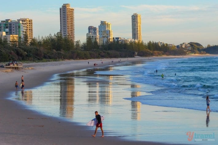 surfer walking out of ocean at burleigh heads with skyrises in the background