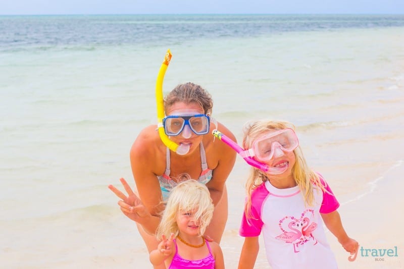 woman and girls posing to camera on beach with snorkels on