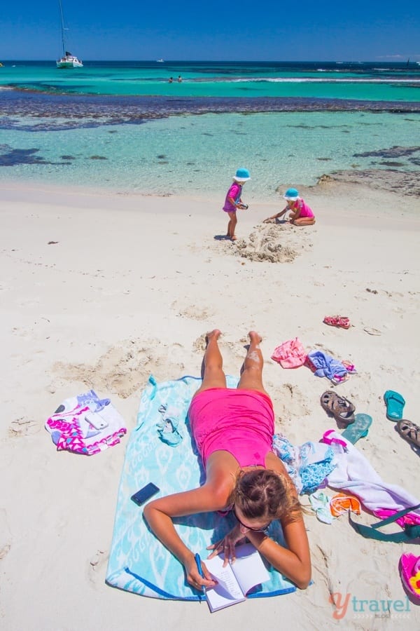 Woman lying on a towel on the beach while children build a sandcastle 