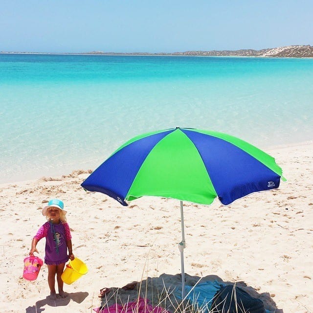 girl standing next to an umbrella on the beach