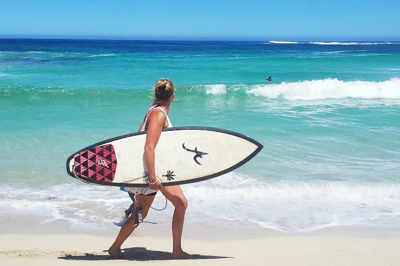 person walking on beach with surfboard under arm 
