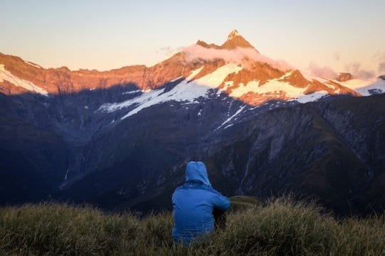 person sitting on a hill looking at a snowy mountain