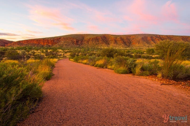 sunrise glow over red dirt road going through valley  