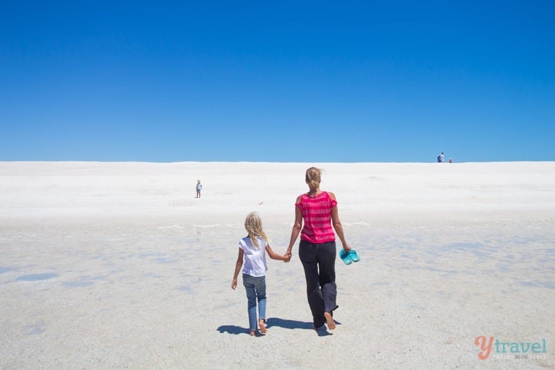 woman and girl holding hands walking on white sand
