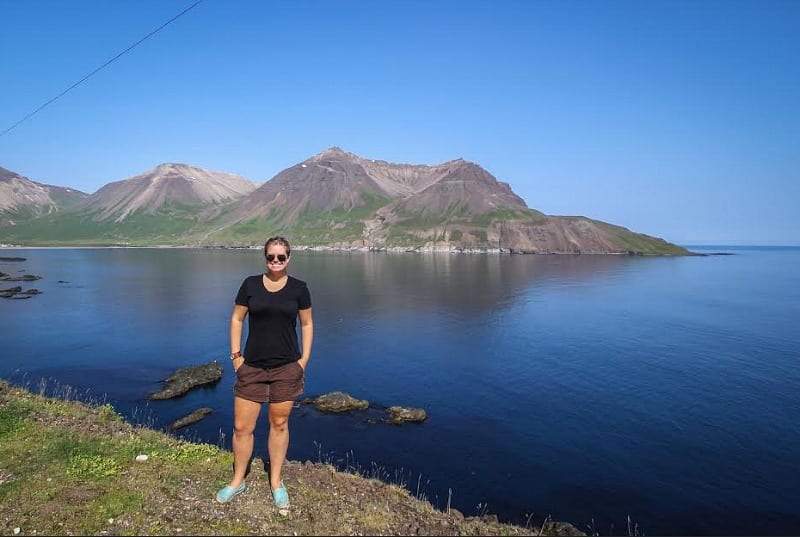 person standing next to a lake with mountains in the background
