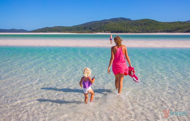 woman and child walking through the water next to a sand island at Whitehaven beach