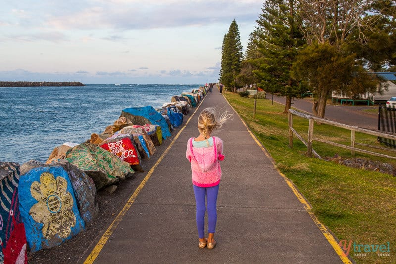 girl walking past colorful painted rocks at the The Breakwall, Port Macquarie, NSW, Australia