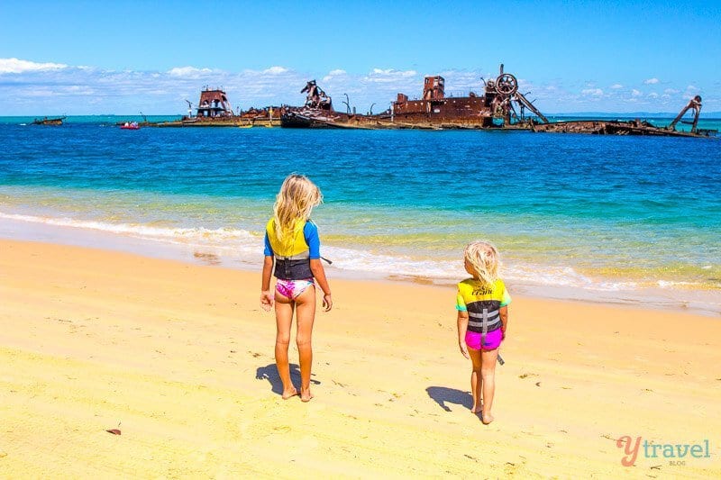two girls on beach looking at shipwreck just offshore