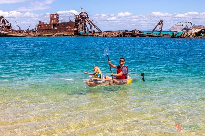 man and child kayaking in clear kayak in front of shipwreck 