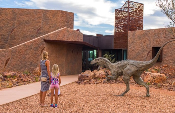 people standing in front of a model of a dinosaur
