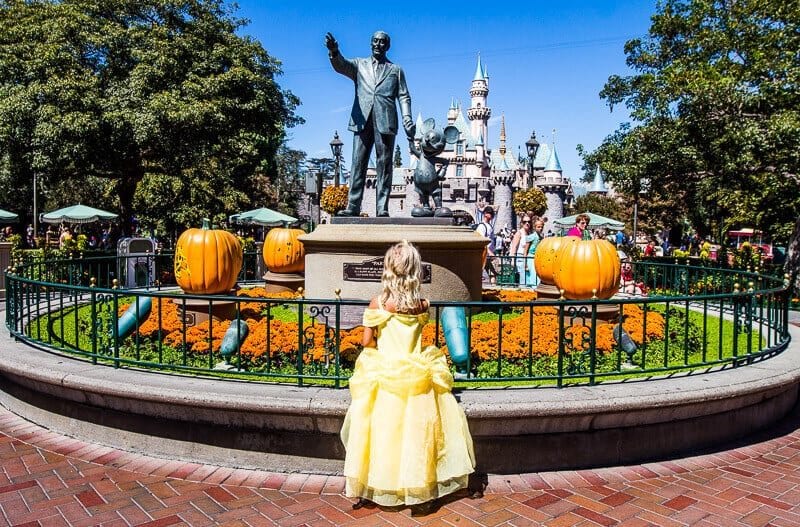 girl in princess dress looking at statue of walt disney and mickey mouse
