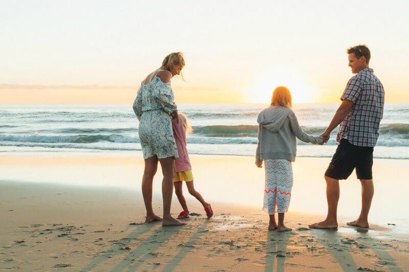 family standing on beach watching sunrise