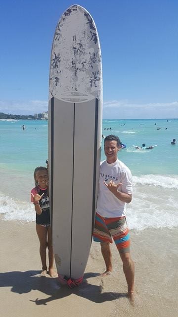 man and girls tadning next to a long board at  Waikiki Beach 