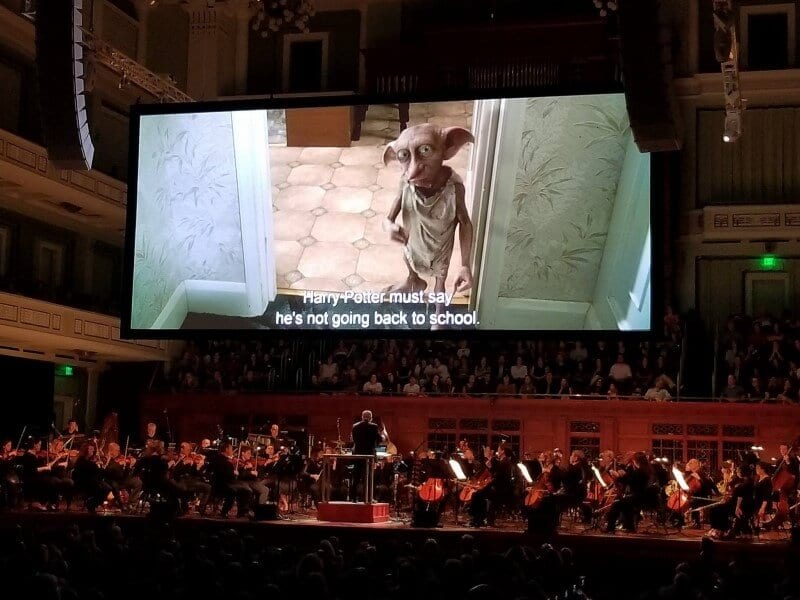 Orchestra playing the score of the Harry Potter movie with dobby on the big screen