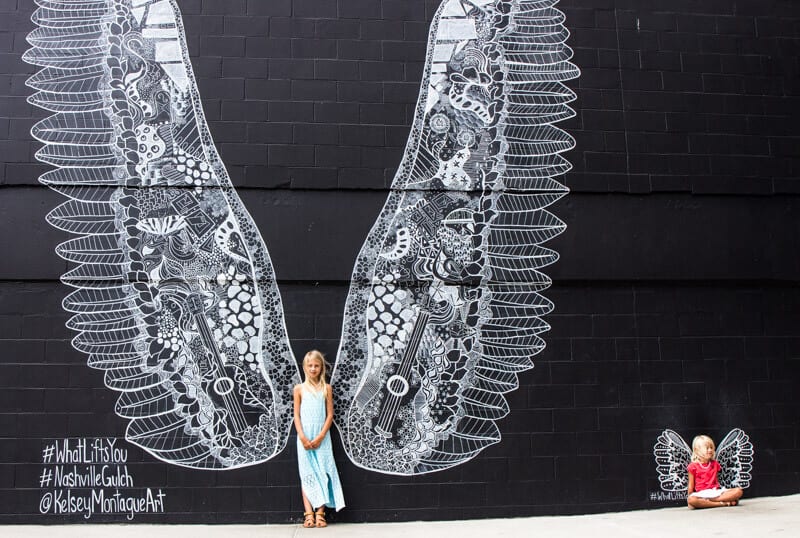 girl standing in front of a wall mural of wings