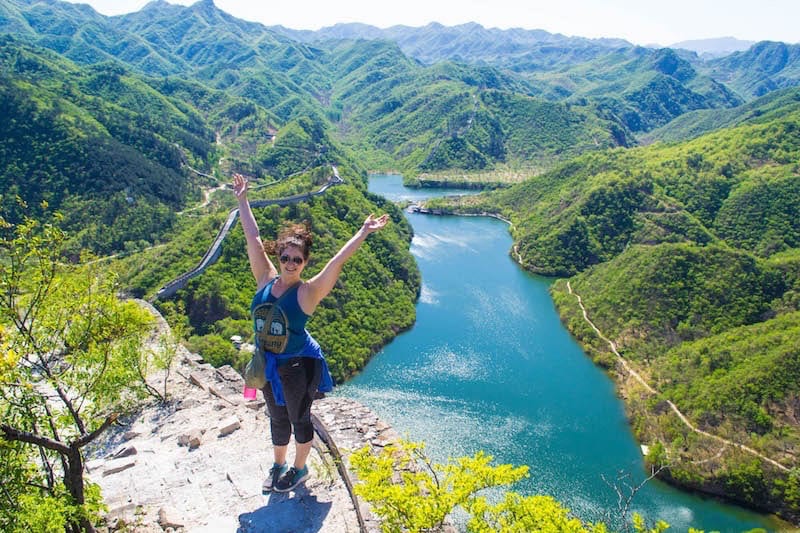 girl with hands in the air in front of lush view of Great Wall of China