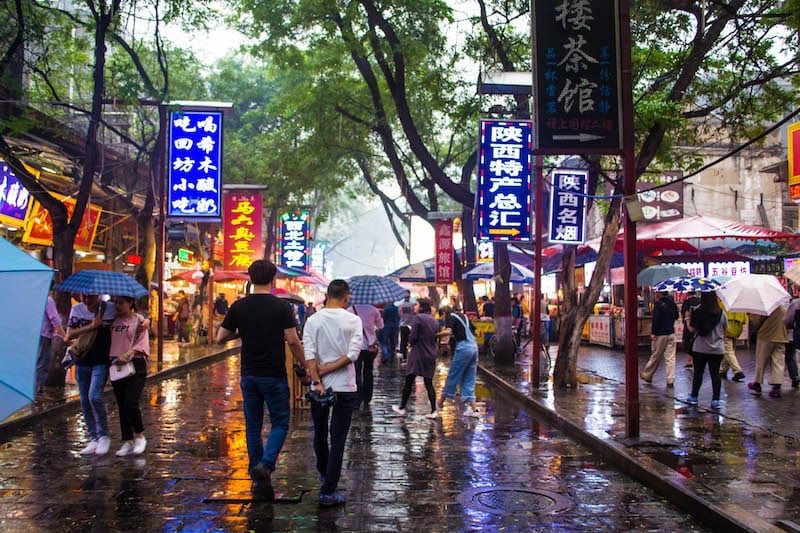 people walking through the Huiminjie Muslim Market in the rain