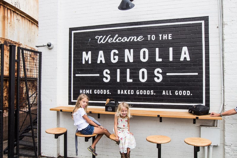 kalyra and savannah sitting under welcome to magnolia silos sign