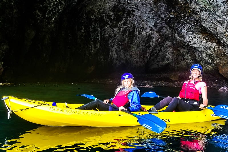 people kayaking next to a cave