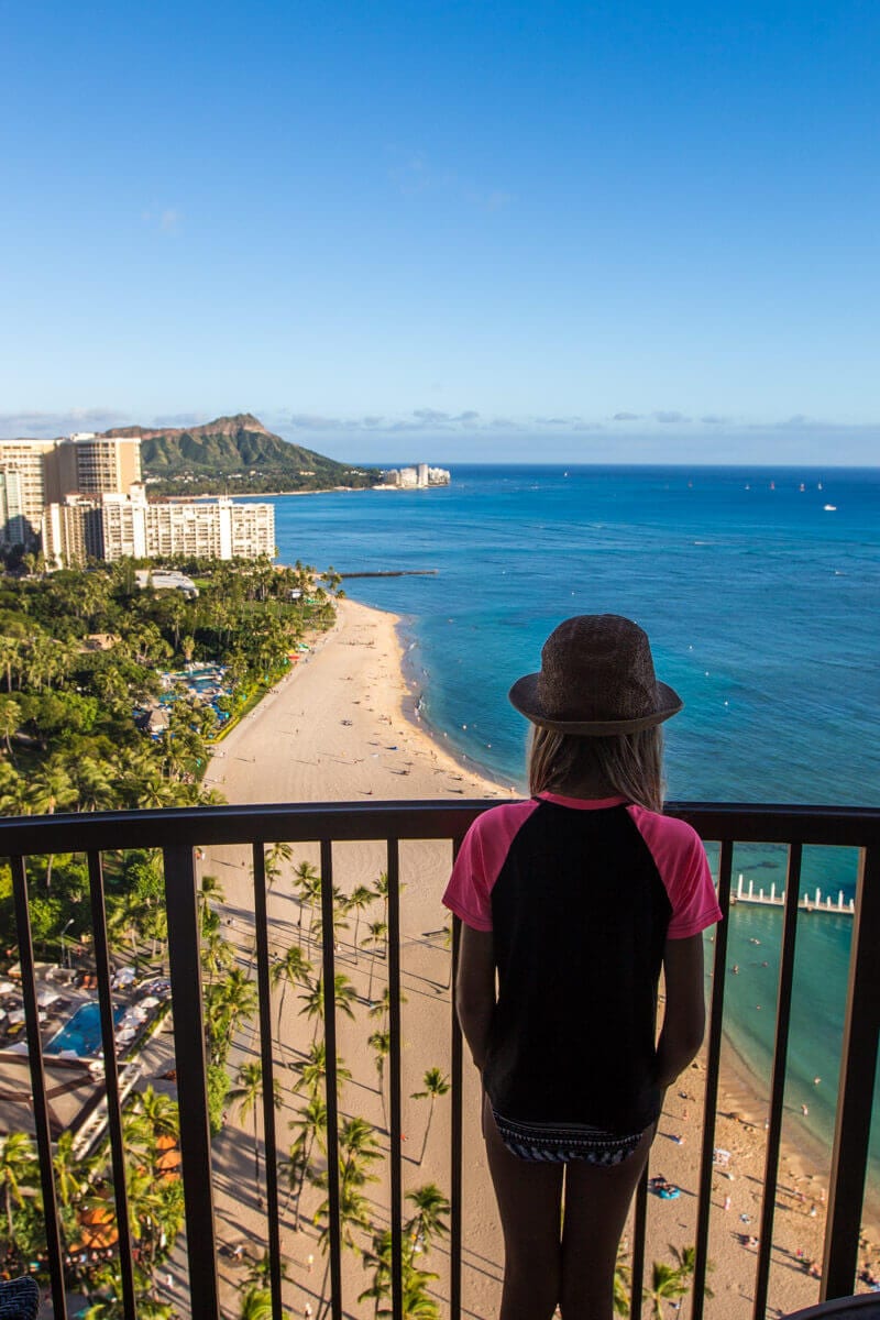 girl on hotel balcony looking at view of waikiki beach with diamond head in distance