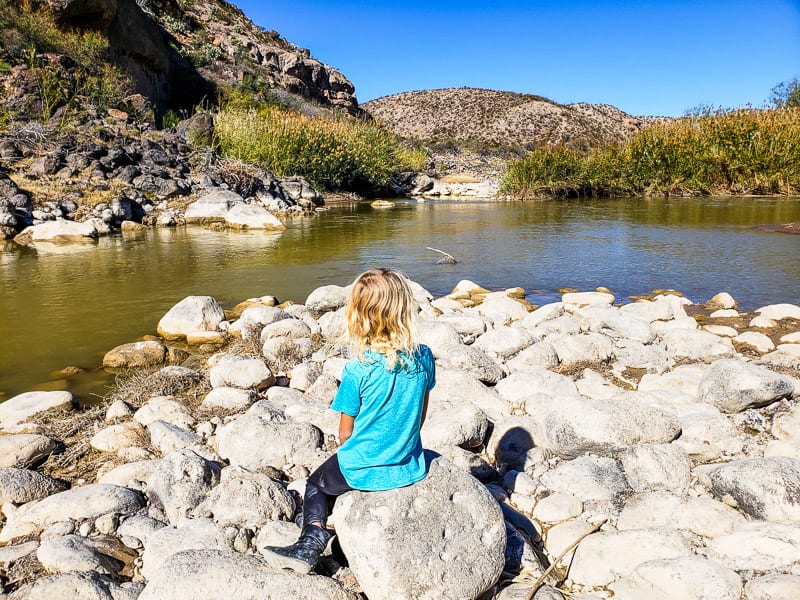 girl sitting on a rock next to a river