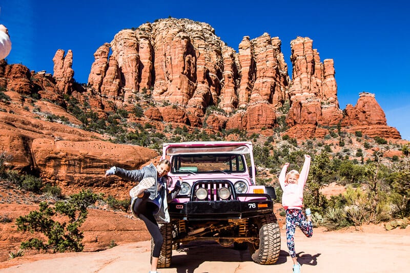 girls jumping in front of Pink Jeep with red rocks behind them