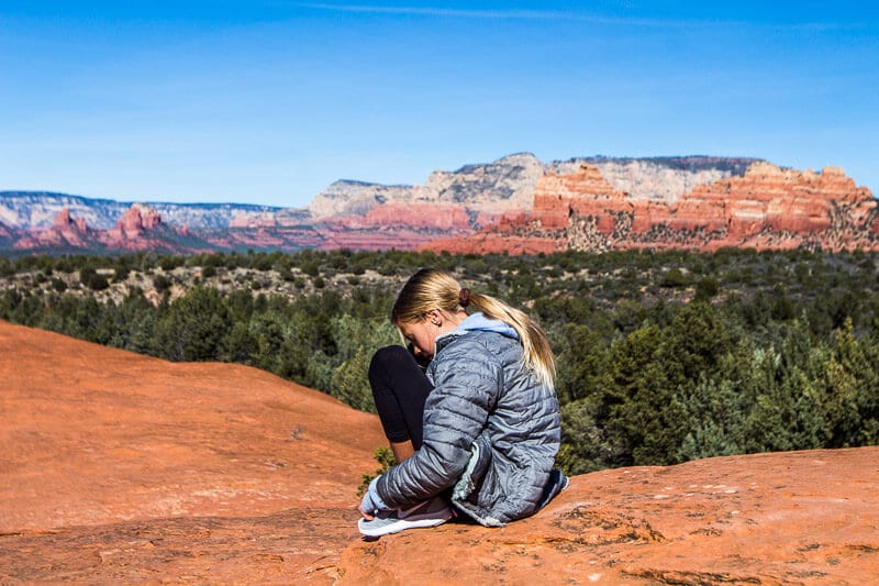 girl sitting on red rock with sedona peaks in background