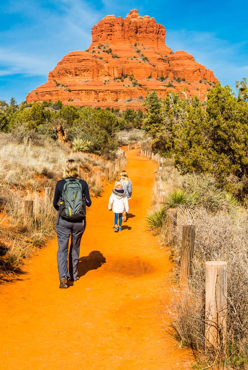 family walking on orange dirt path towards bell rock