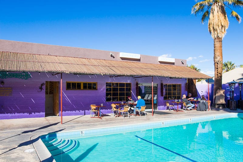 the pool and retro purple building of the 9 Palms Inn at Oasis of Mara